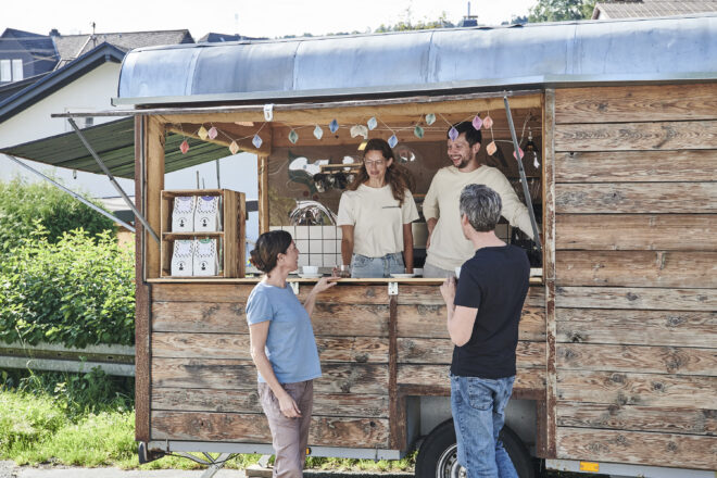 Kaffeeschreiner in ihrem Holz Kaffeeverkaufswagen im Gespräch mit zwei KundInnen